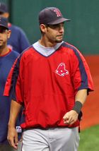 A white male baseball player with facial hair, wearing a blue cap with a red "B" on it, a red polyester shirt, and white pants, looks to his left.