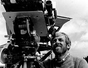 Black and white photograph; a man squints into the telescopic eyepiece of a large mechanical device.