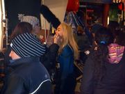Blond woman having make-up applied on a movie set, surrounded by busy people.
