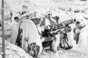A cannon wears a white blanket on the snow and two men pose side of it.