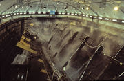 A diagonal section of a wooden ship is lying on its side steel frame at an angle, being sprayed with water from dozens of sprinklers