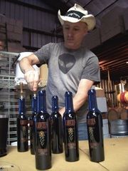 A man inside of a brewing factory stands at a table while corking a blue bottle.