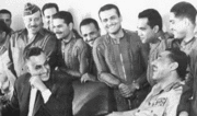 Men in suits laughing, with two of them sitting and looking at each other.
