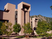 A series of brown boxlike buildings stand in front of a mountain.
