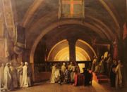 Painting of dozens of men in white robes in a domed chapel.  A young man with short black hair and dark blue robe is kneeling on a stool in the center, and pointing at something in a large open book which is being held by one of the white-robed men.