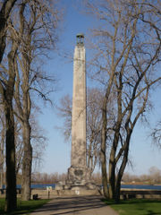 A tall, stone column at the end of a sidewalk, with leafless trees on either side of the sidewalk.